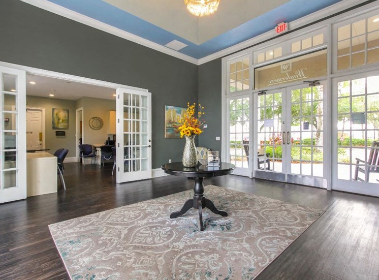 Clubhouse Foyer with a Table in the Middle with A Vase and Flowers on it Hardwood Floors Large Windows and Open Doors Leading to Clubhouse Seating Area